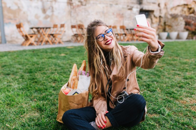 femme assise dans l'herbe fait un selfie