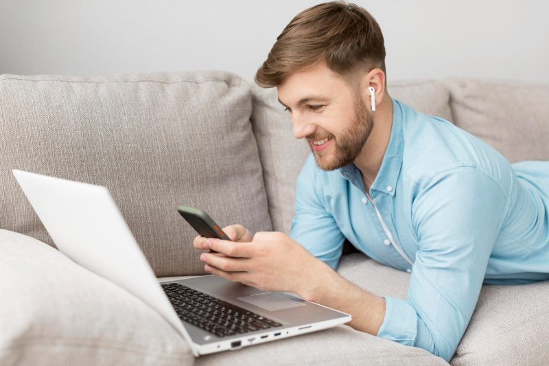 homme allongé devant son pc avec ses airpods dans les oreilles