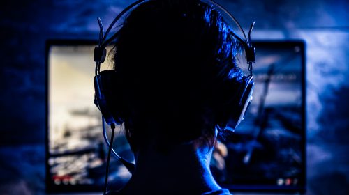 gamer pris de dos avec un casque de jeu qui joue a un jeu vidéo dans la pénombre
